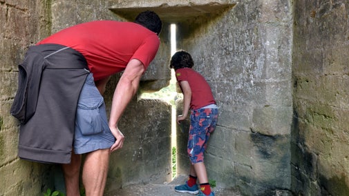 Man and boy peering through an arrow loop at Corfe Castle